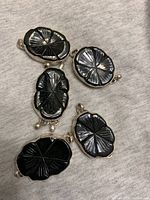 Five black spinel pendants with carved radial patterns laid out on a light fabric background, each showing unique carving details and silver-tone frames.