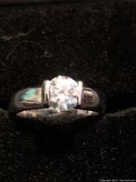 Front view of the silver ring showing the round moissanite center stone with bezel setting on a black background.