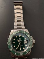 Front view of diver watch showing green bezel and green dial with luminous markers, date with magnifier, and stainless steel bracelet.