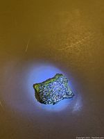 Green Moldavite gemstone piece with rough, textured surface under lighting, highlighting its glassy and reflective qualities.