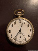 Front view of pocket watch showing white dial, black Arabic numerals, blued-steel hour and minute hands, small seconds hand