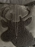 Photo of the silver chain necklace with a small spherical meteorite pendant against a soft dark pillow with a deer head pattern.