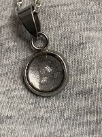 Close-up of round meteorite pendant showing the fragment under glass cover.