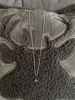 Full view of silver chain necklace with round pendant displayed on a textured dark fabric background.