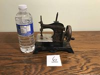 Front view of the antique German toy sewing machine next to a water bottle to show scale.