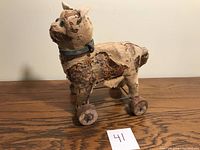 Side profile of antique cat pull toy showing cloth worn exterior, straw filling, wooden wheels, and metal wheel base.