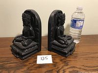 Side view of one Asian deity bookend next to a water bottle for scale, showing the thick material and detailed carving.