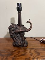 Side view of bronze peacock lamp base with detailed feather design and lamp socket on top, no shade.
