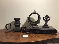 Overview of five heavy cast iron and brass decorative pieces displayed on wooden surface against plain wall.