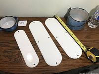 Front view of three enamelware sign plates white front, varying sizes from small to large with handle and bowl on the side.