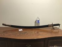 Full side view of the sword in its scabbard showing length and shape, bottle shown for scale.