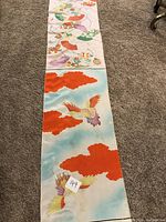 Photo showing kimono silk fabric with colorful birds and bright red cloud patterns on a light blue background, laid out on carpeted floor.