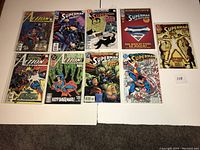 Photo of nine Superman-related comic books in sleeves laid out in two rows on a white surface. Covers show various comic scenes and characters.