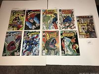 Photo showing nine comic books in protective sleeves laid out on a white surface. Various Superman-related titles featured with colorful illustrated covers.