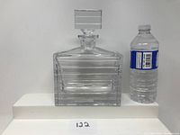 Front side view of the Mikasa Latitudes crystal decanter next to a water bottle for scale, showing horizontal lines detail and the square stopper.