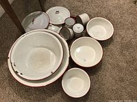 Overview of the enamelware lot showing large and small bowls, multiple lids, and signs of wear/chipping on rims.
