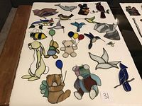 Photo showing 21 stained glass animals and bird pieces arranged on white surface, including bears, birds, bees, whales, rabbit and fish.