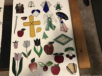 Full top-down view of 25 assorted stained glass pieces arranged on white boards on carpet and wooden table.
