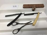 Full set of vintage barber utensils including two straight razors, ornate scissors, and a textured case.