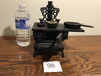 Front view of vintage cast iron salesman's stove with door open and accessories on top, water bottle for size reference.