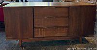 Front view of mid-century style wood veneer credenza cabinet showing three center drawers and two side doors on tapered legs