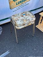 Front view of a single chair showing metal legs and heavily worn cushion with paint spots.