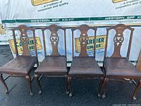 Four vintage dark wooden dining chairs with carved backs and upholstered seats, shown side by side.