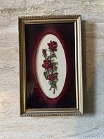 Framed cross stitch featuring red roses on white fabric with gold frame