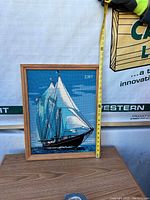 Framed sailboat cross stitch artwork with measuring tape held vertically showing approximately 17 inches height.