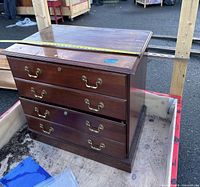 Front and top view of the wooden dresser showing four drawers with brass handles and measuring tape on top showing measurements.