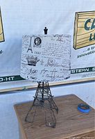 Full view of the Eiffel Tower-shaped table lamp on a wooden surface against a fabric backdrop with text.