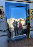 Frontal image of rectangular wall mirror with glass frame showing reflective surface and frame design against outdoor background.