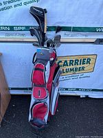 Golf set with clubs inside a golf bag, against a building exterior with lumber signage.