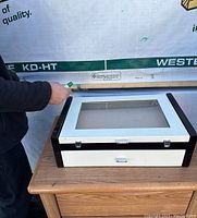 Image of the jewelry/safety box on a small wooden table, showing closed glass lid and metal clasps on the front.