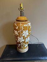 Front view of brown ceramic lamp showing white floral and bamboo relief design