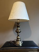 Full view of the brass table lamp showing the white floral patterned lampshade and polished brass base with power cord.