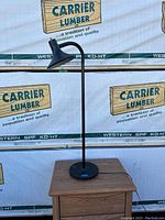 Full view of the single black floor lamp post showing round base, vertical pole, and angled cone-shaped shade