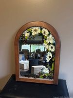 Front view of arched wooden framed mirror with stained glass floral design on reflective surface.