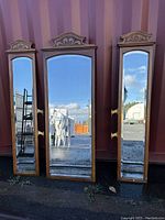 Front view of three wood framed mirrors with arched tops and carved crest decorations, positioned against container.