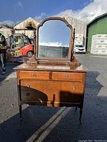 Frontal view of the old style maple dresser with two smaller drawers on top and five larger drawers below. Central mirror is large with a top curved frame and wood supports on each side.