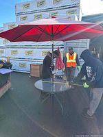 Outdoor round glass table with green metal frame and red umbrella set up outside.