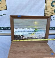 Framed painting of ocean sunset with tape measure showing 28 inches width