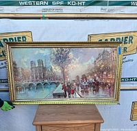 Full view of framed oil painting with Paris street scene and Notre Dame Cathedral in background, purple-blue sky with pedestrians and carriage by river.
