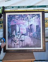 Front view of framed painting held by gloved hands with size measuring tape showing approx 42 inches.