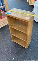 Photo showing front and side of the wooden 3 shelf cabinet with a tape measure across the top width measurement.