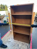 Photo shows front of wooden shelving unit with a person measuring width of 28 inches.