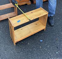 Wooden shoe rack with measuring tape stretched across width showing approximately 24 inches.