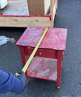 Red wooden side table shown with measuring tape on top to indicate width about 25 inches on tabletop.
