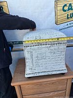 Storage stool with French script upholstery, tape measure showing width around 16 inches