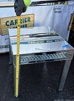 Full view of the square glass top table with mirrored legs. Table height shown by measuring tape is approximately 24 inches.